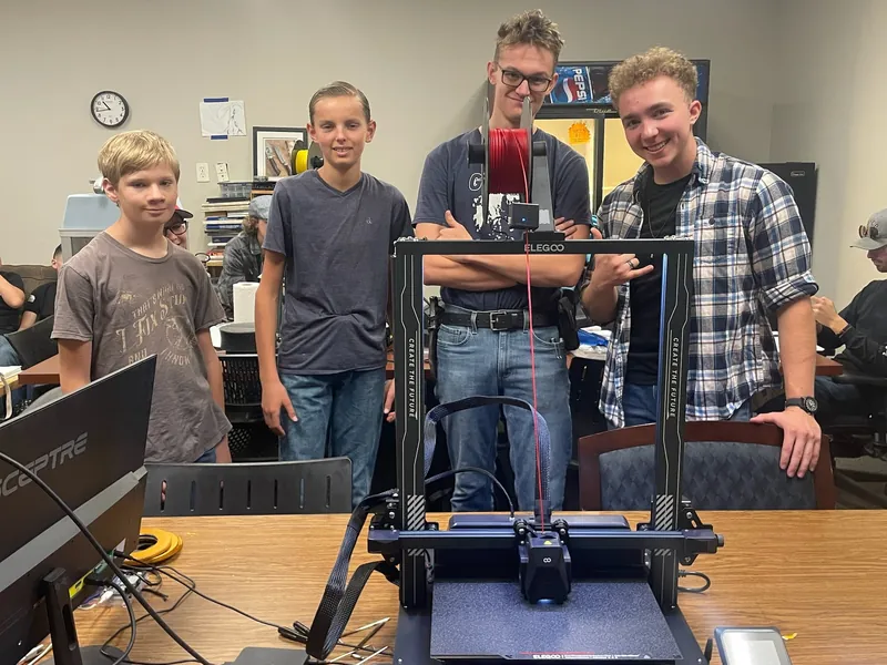 Four students gathered around a desktop 3D printer in the shop.